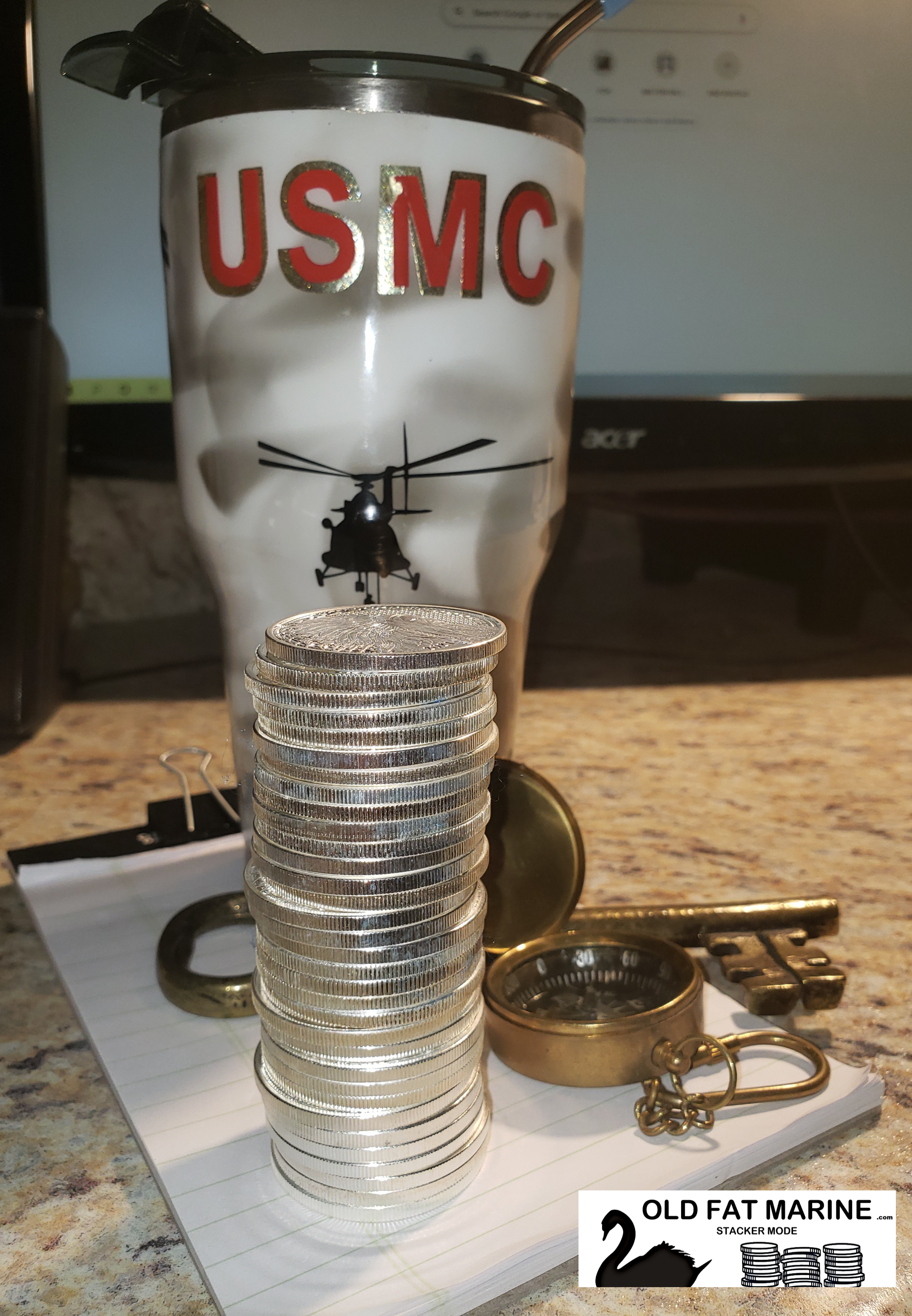 A photo of a homemade 32 ounce tumbler with USMC letters and a decal of a helicopter that appears to be hovering over a stack of silver coins that is placed in front of the tumbler.