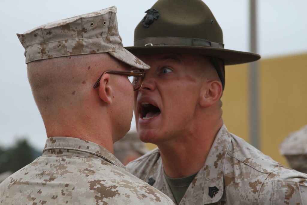 A photograph of a U.S.M.C. Drill Instructor screaming in the face of a recruit.