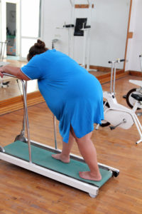 An overweight woman exhausted trying to walk on a treadmill.