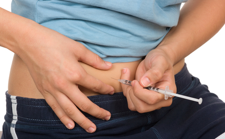 A close up photo of a woman giving herself an insulin shot in the abdomen.  