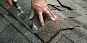 a close up view of a person hammering a roofing shingle on a rood cap.